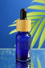 Photo of Bottle of face serum on wet surface against blue background, closeup