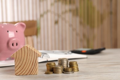 House model, stacked coins, piggy bank and notebook on wooden table, selective focus