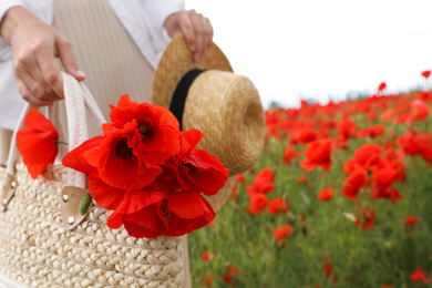 Photo of Woman holding straw hat and handbag with poppy flowers in beautiful field, closeup