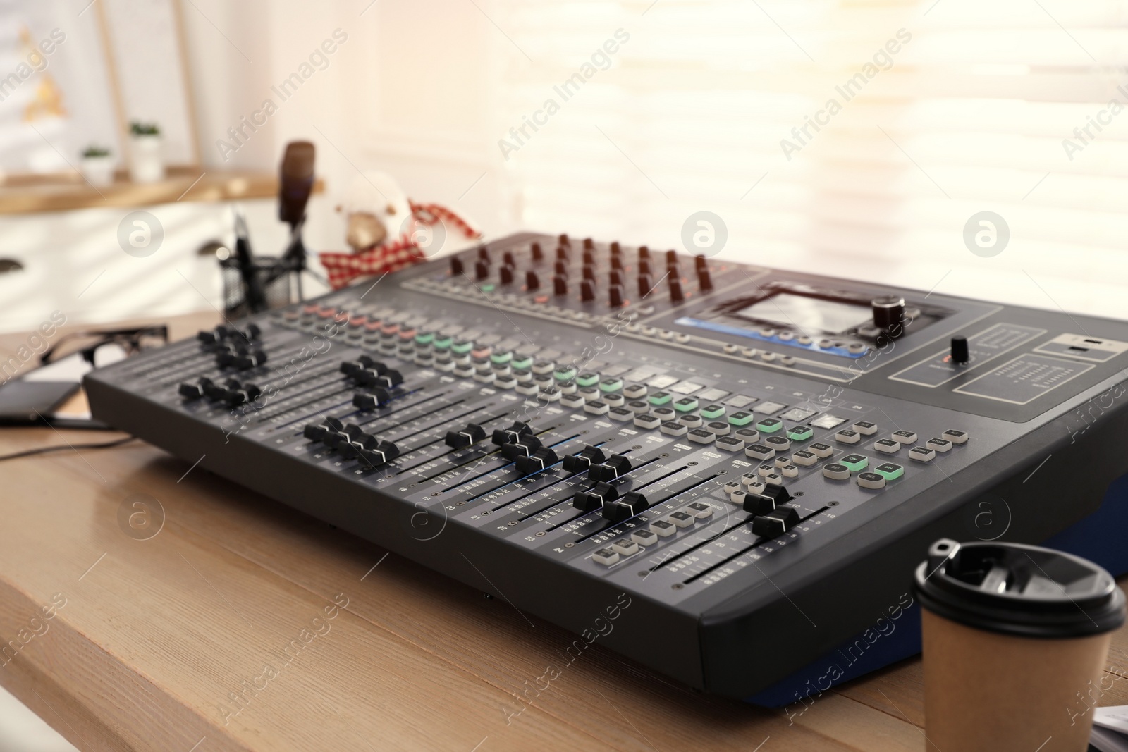 Photo of Professional mixing console on wooden table in modern radio studio