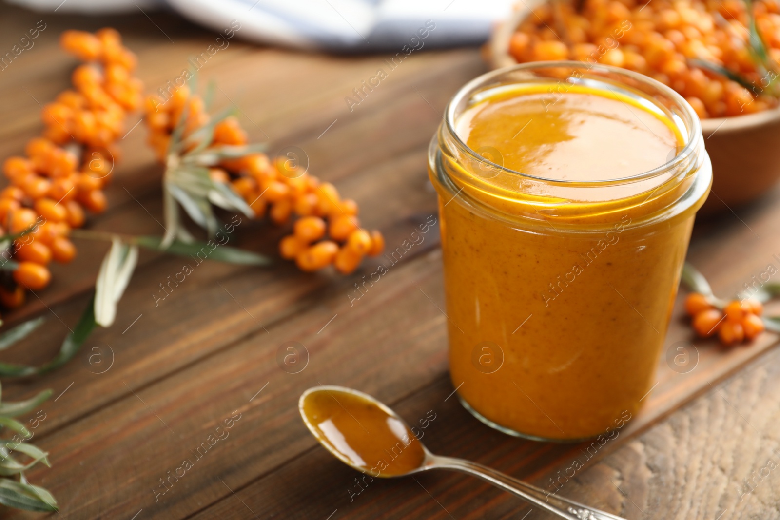 Photo of Delicious sea buckthorn jam and fresh berries on wooden table. Space for text