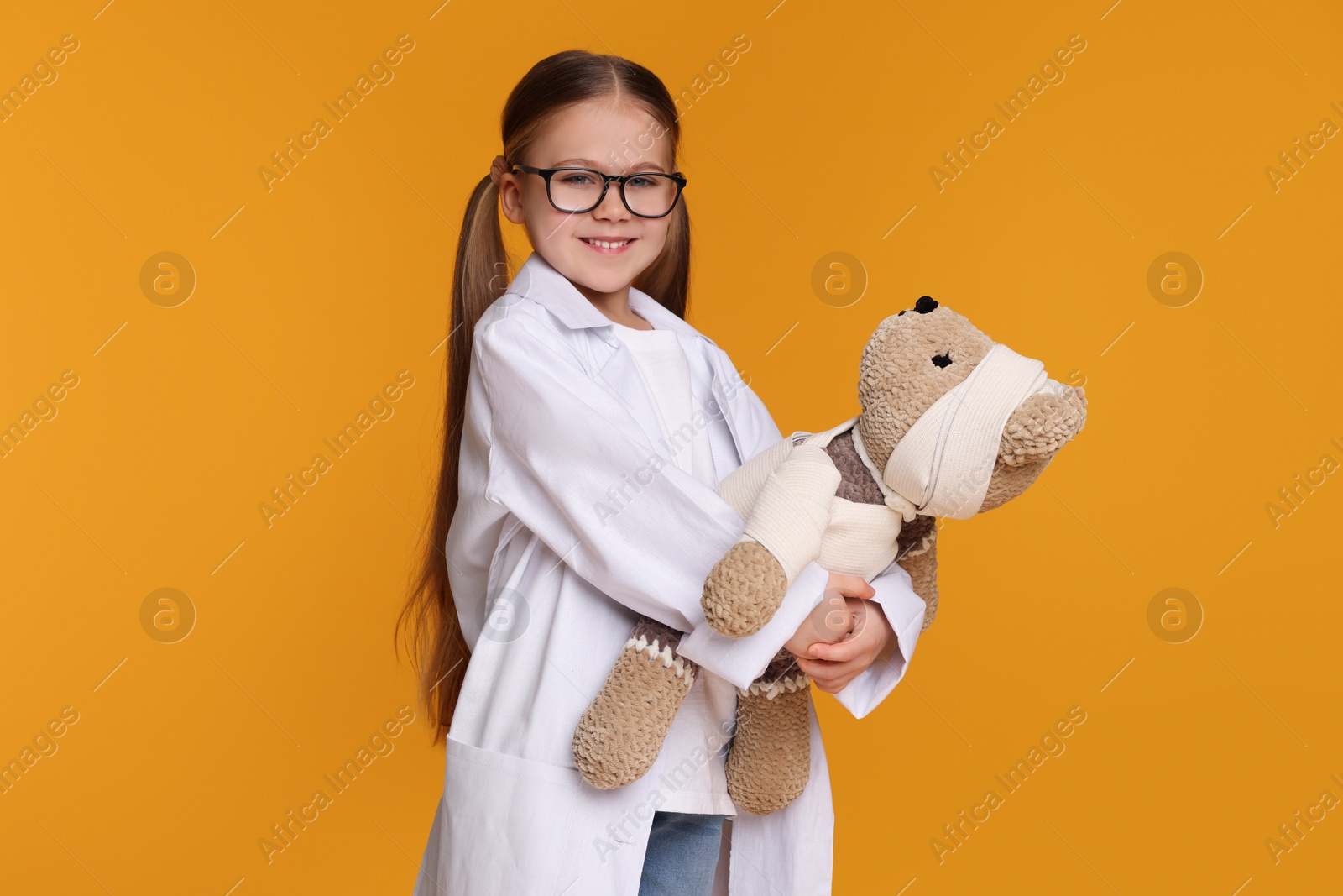 Photo of Little girl in medical uniform with toy bear on yellow background