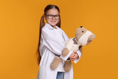 Photo of Little girl in medical uniform with toy bear on yellow background