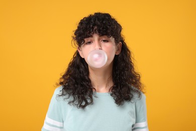 Beautiful young woman blowing bubble gum on orange background