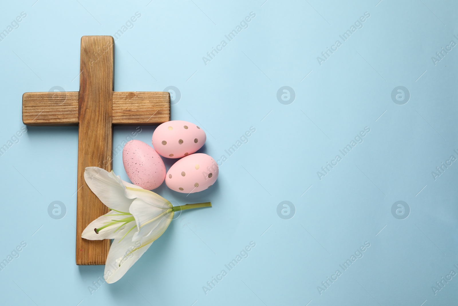 Photo of Wooden cross, painted Easter eggs and lily flower on light blue background, top view. Space for text