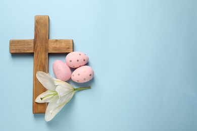 Wooden cross, painted Easter eggs and lily flower on light blue background, top view. Space for text