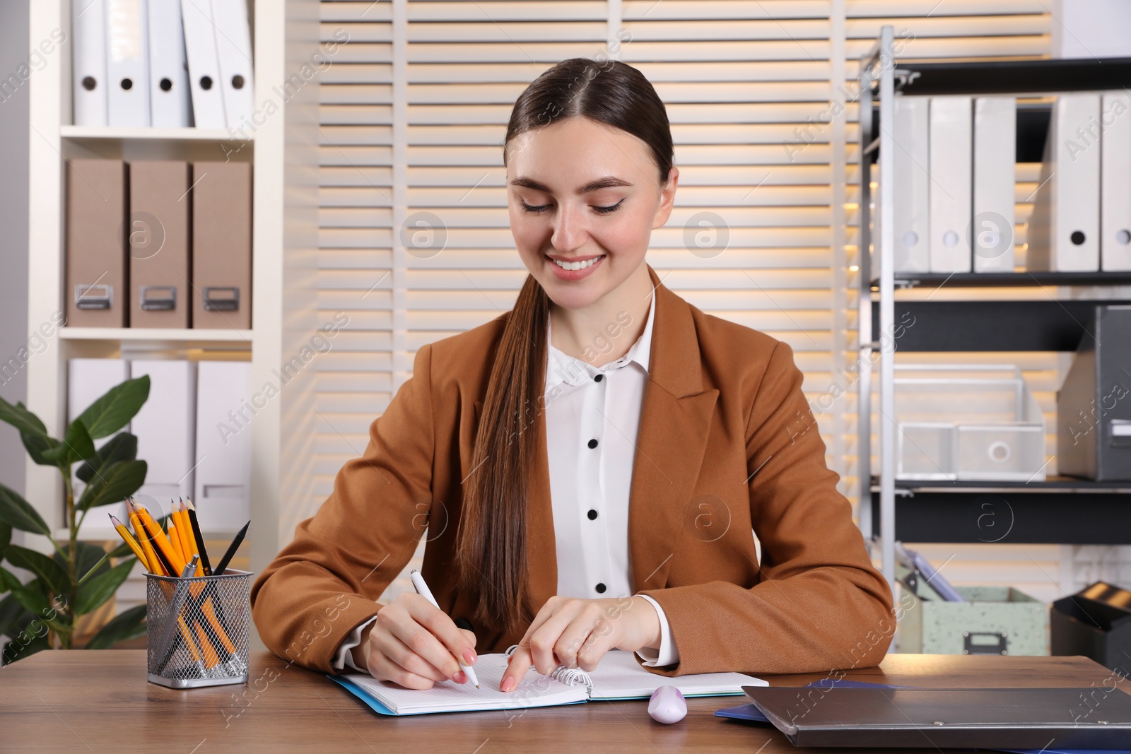 Photo of Happy woman taking notes at wooden table in office