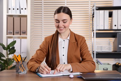 Happy woman taking notes at wooden table in office