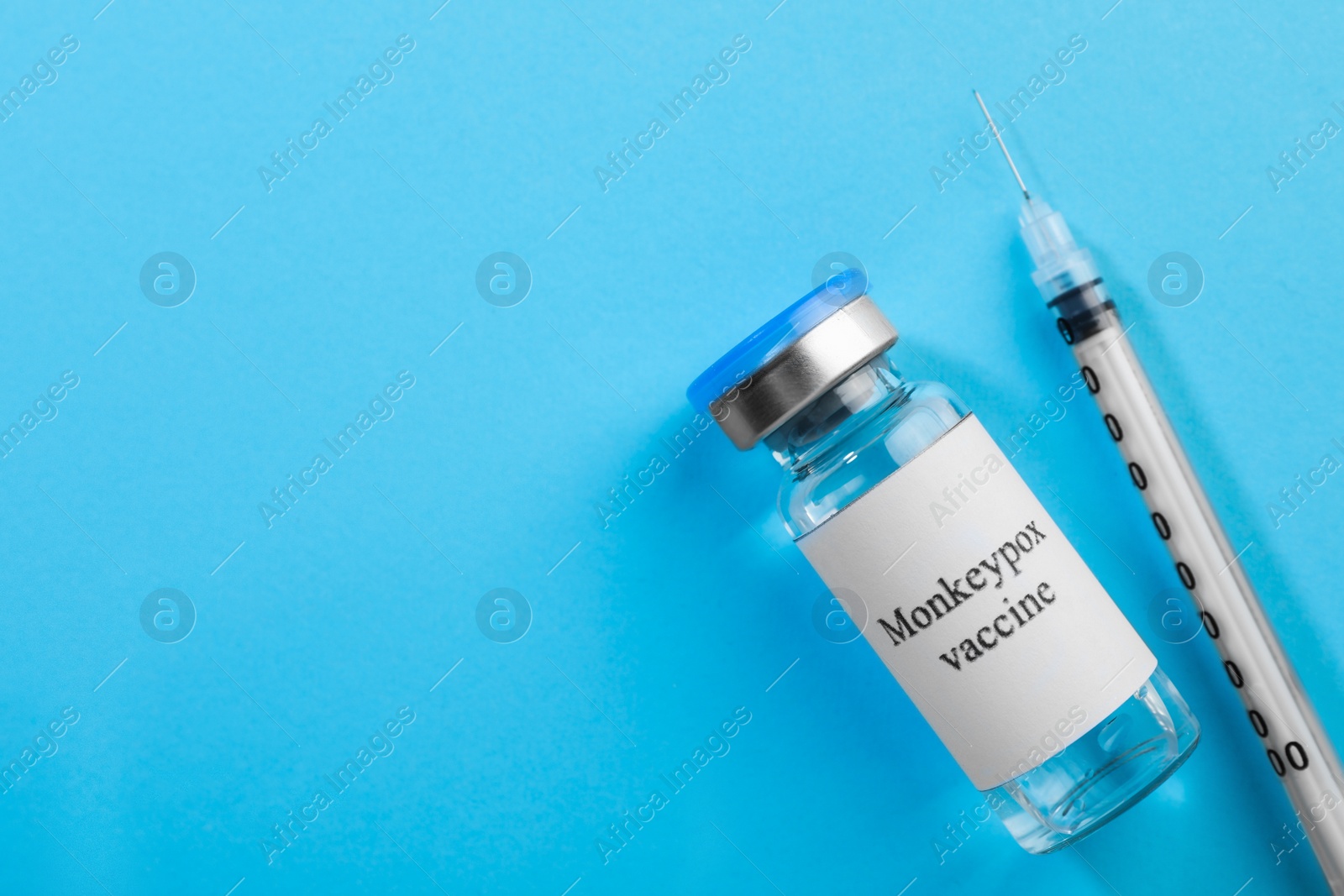 Photo of Monkeypox vaccine in glass vial and syringe on light blue background, flat lay. Space for text