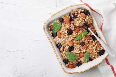 Photo of Tasty baked oatmeal with berries and almonds in baking tray on white textured table, top view. Space for text