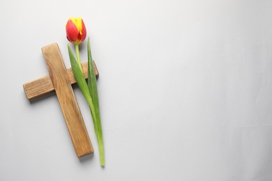 Easter - celebration of Jesus resurrection. Wooden cross and tulip on light background, top view. Space for text