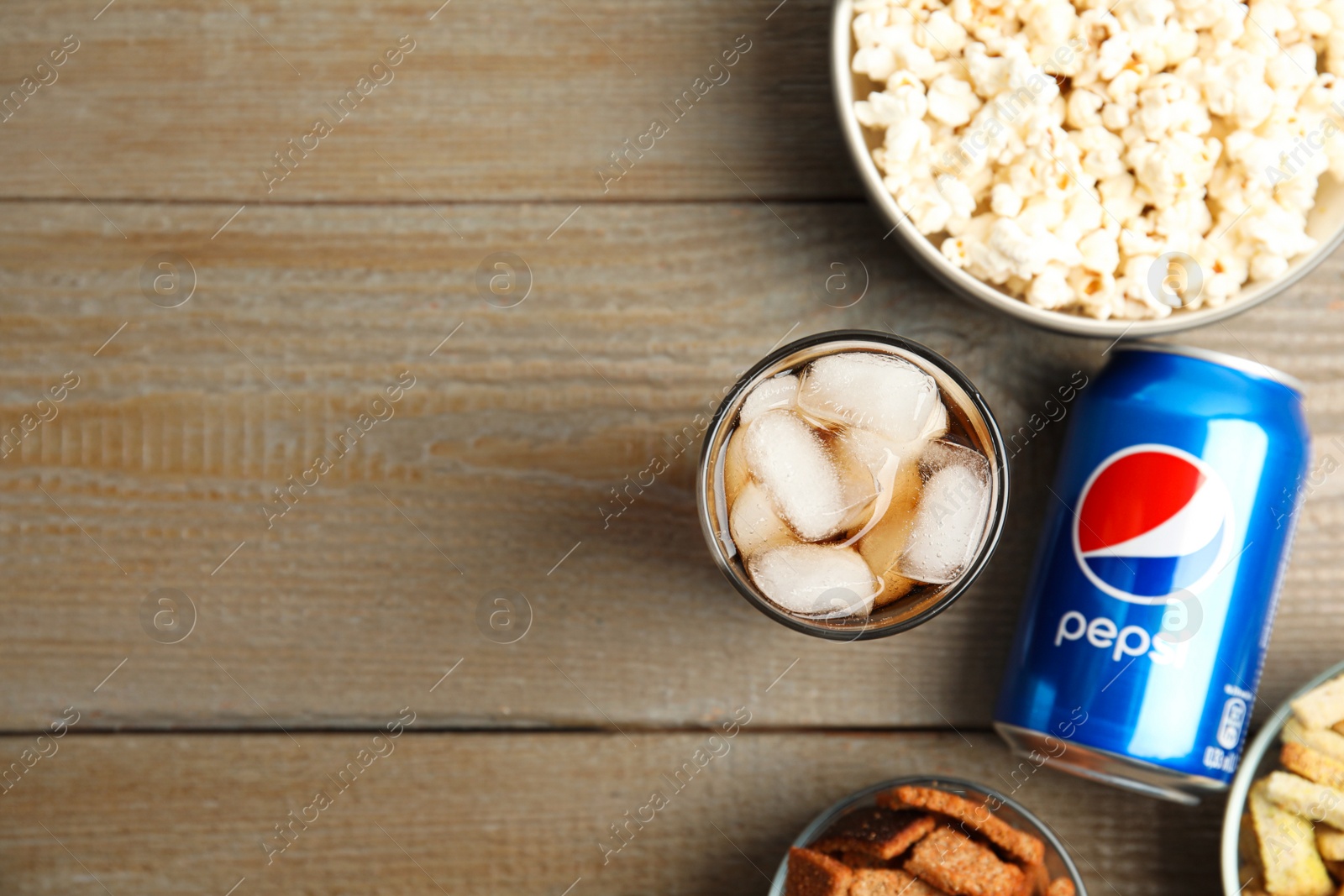 Photo of MYKOLAIV, UKRAINE - FEBRUARY 15, 2021: Glass of Pepsi, can and snacks on wooden table, flat lay. Space for text