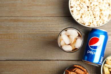 MYKOLAIV, UKRAINE - FEBRUARY 15, 2021: Glass of Pepsi, can and snacks on wooden table, flat lay. Space for text