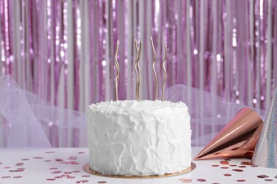 Delicious cake with candles and party hats on white table