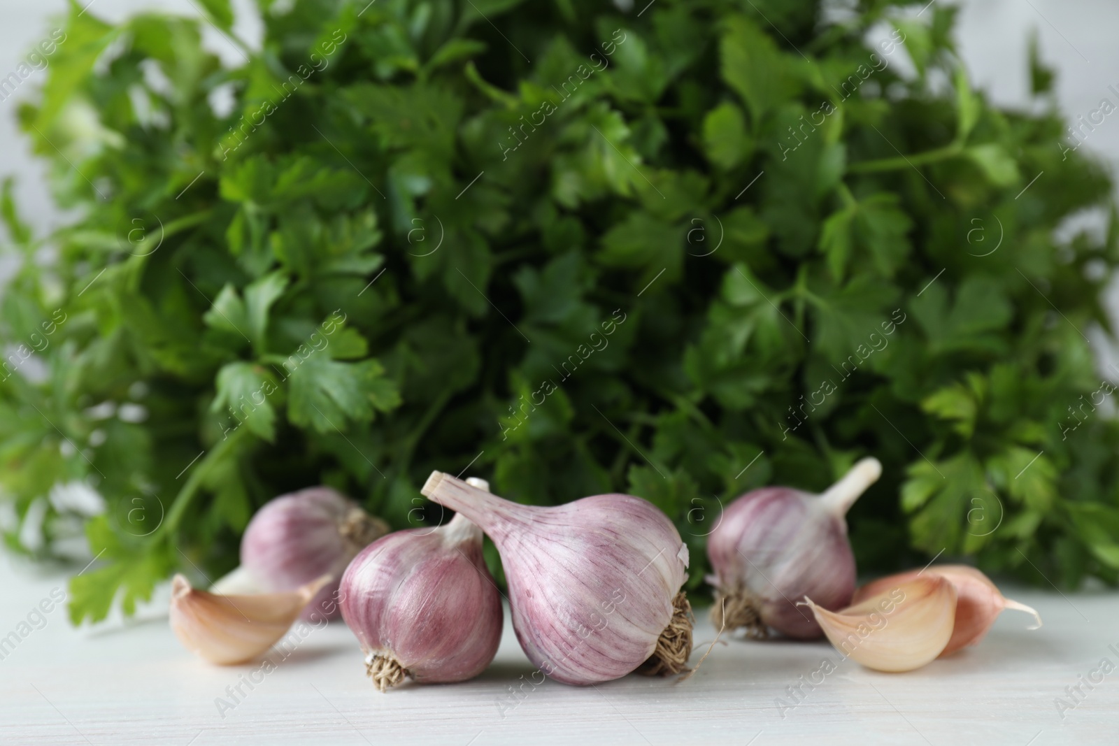 Photo of Fresh raw garlic and parsley on white wooden table, closeup