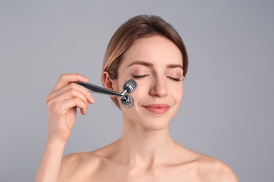 Young woman using metal face roller on light grey background