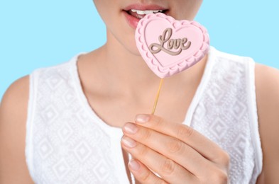Woman eating heart shaped lollipop made of chocolate on light blue background, closeup