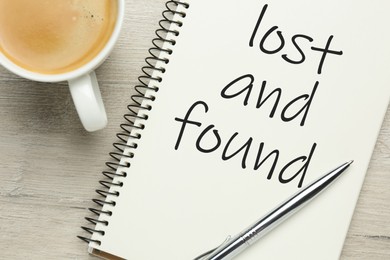Image of Notebook with phrase Lost and Found, cup of coffee and pen on white wooden table, flat lay