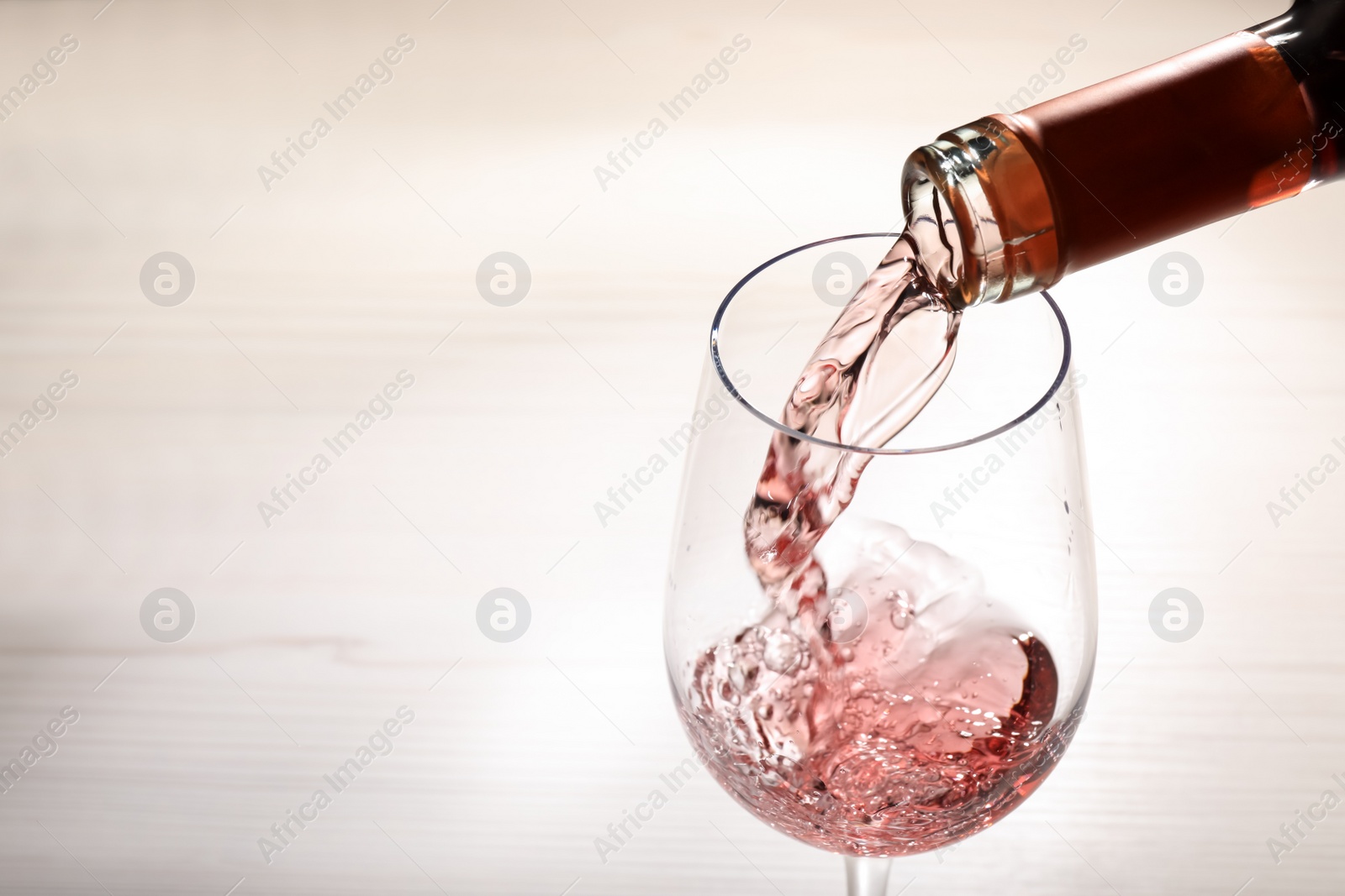 Photo of Pouring rose wine from bottle into glass on wooden table, closeup. Space for text