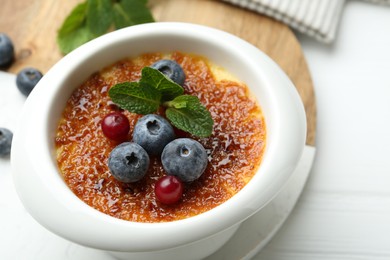 Photo of Delicious creme brulee with berries and mint in bowl on white table, closeup