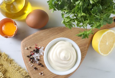 Photo of Tasty mayonnaise sauce in bowl, ingredients and spices on white table, flat lay