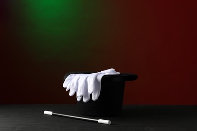 Photo of Magician's hat, wand and gloves on black wooden table against dark background, space for text