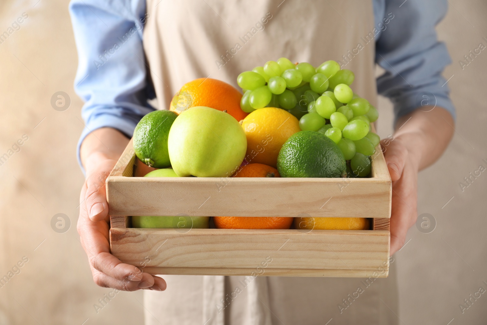 Photo of Woman holding wooden crate with fresh fruits on color background, closeup