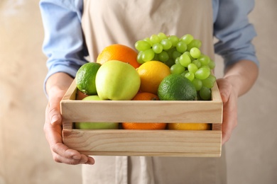 Photo of Woman holding wooden crate with fresh fruits on color background, closeup