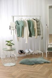 Rack with stylish warm clothes and shoes near mirror in dressing room