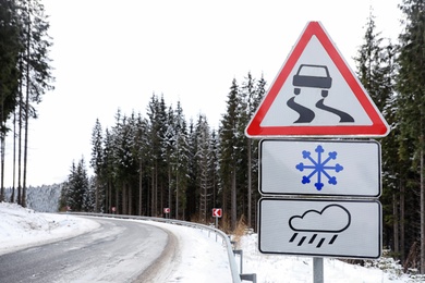 Warning traffic signs near snowy road through forest. Winter driving