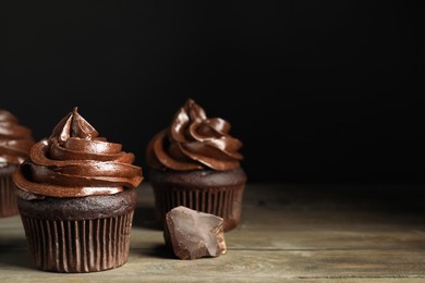 Delicious chocolate cupcakes with cream on wooden table against dark background. Space for text