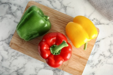 Wooden board with ripe paprika peppers on marble background, top view