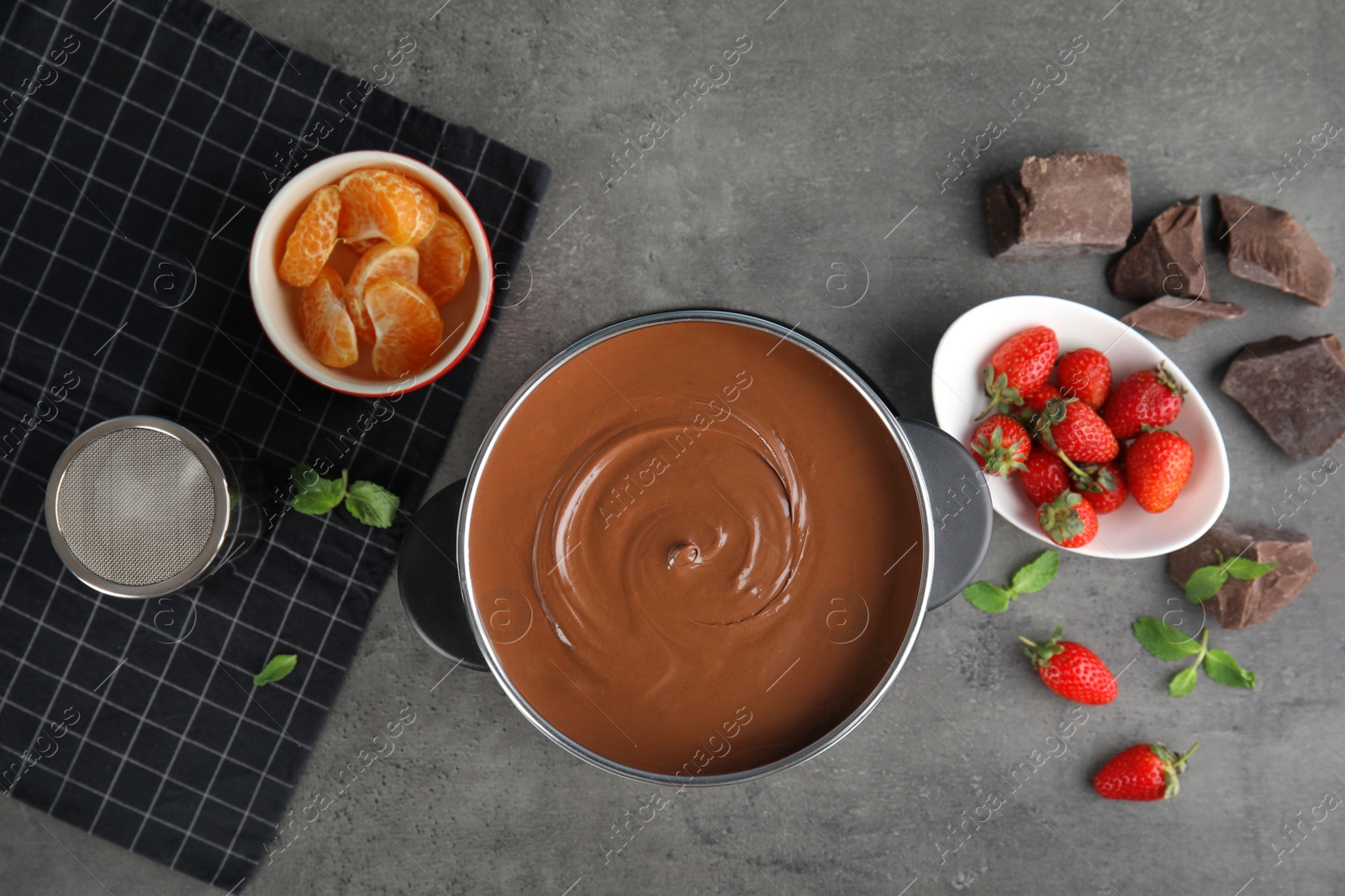 Photo of Flat lay composition with chocolate fondue in pot and fruits on gray background