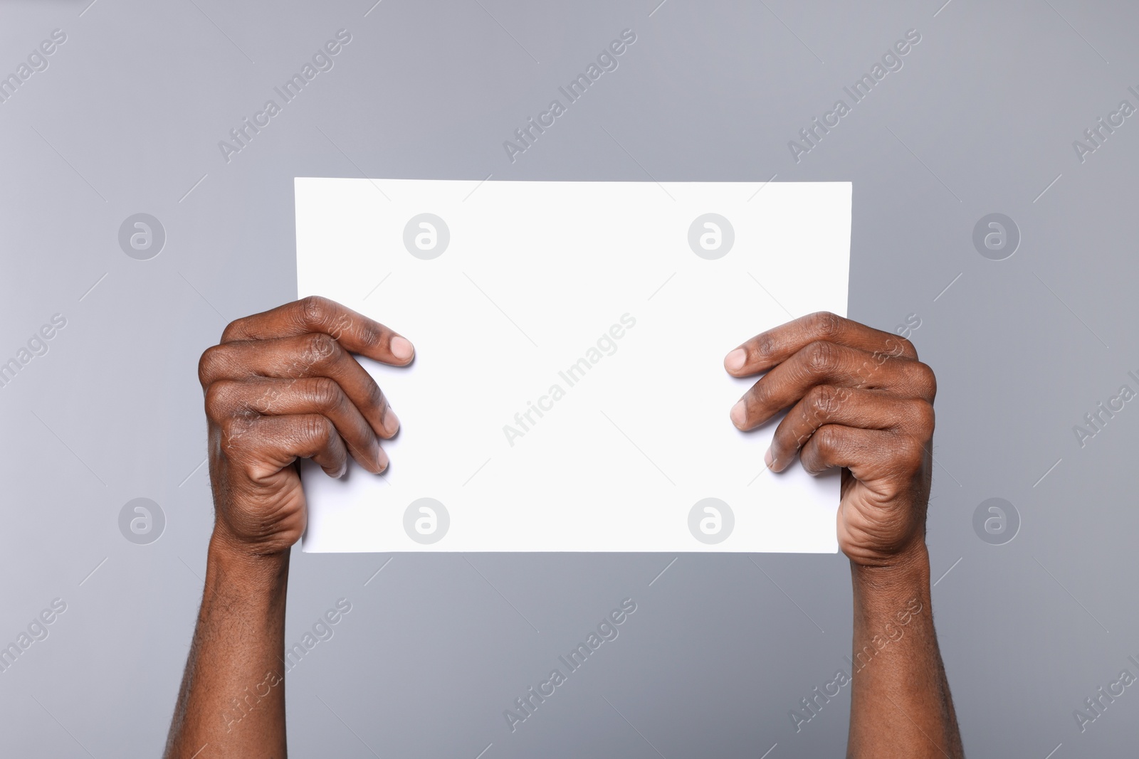 Photo of African American man holding sheet of paper on grey background, closeup. Mockup for design