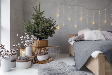 Photo of Little Christmas tree with fairy lights in bedroom interior