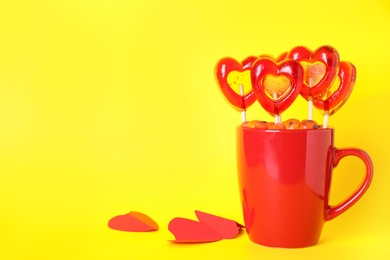 Photo of Cup with different candies on yellow background, space for text