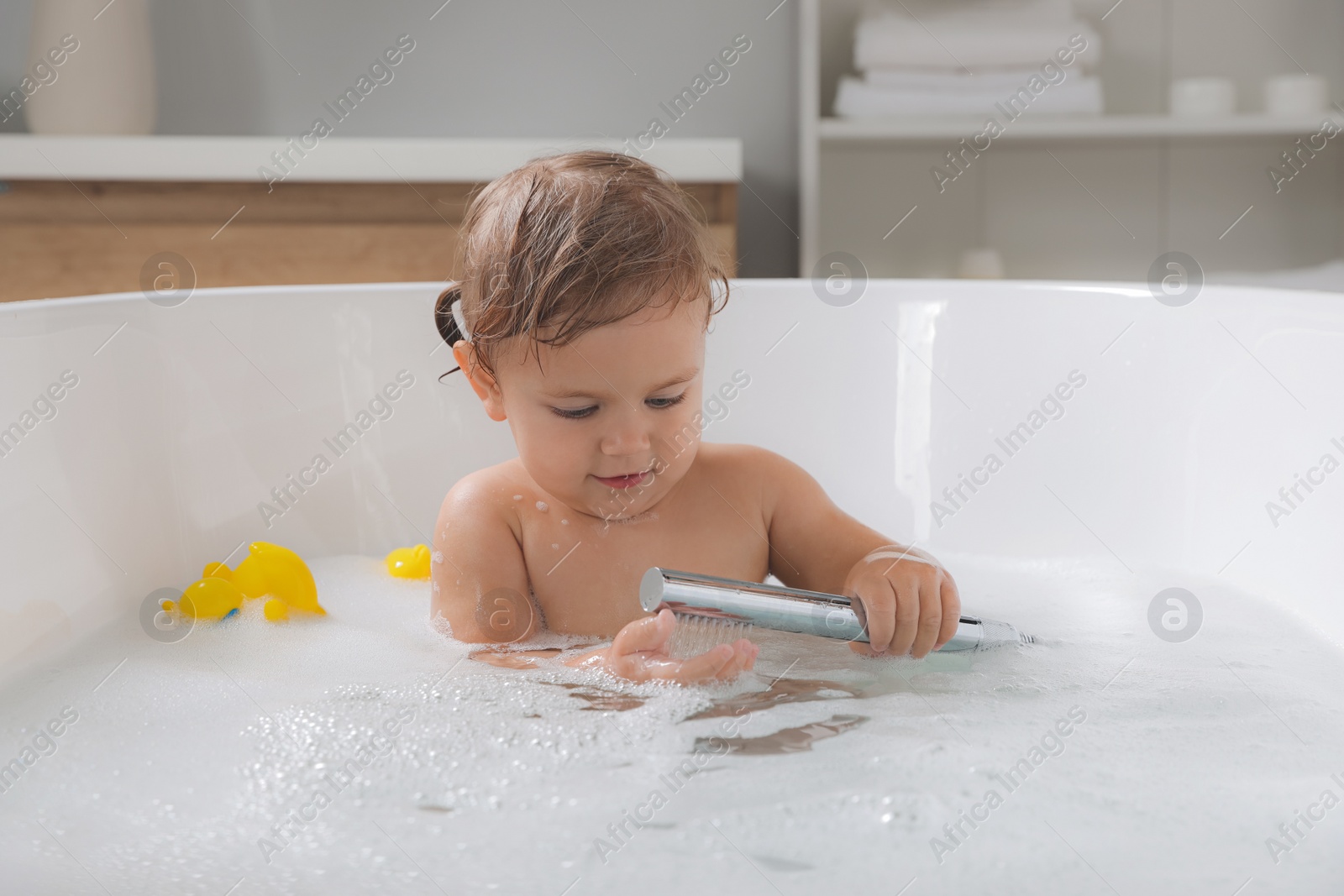 Photo of Cute little girl playing with shower head in bathtub at home