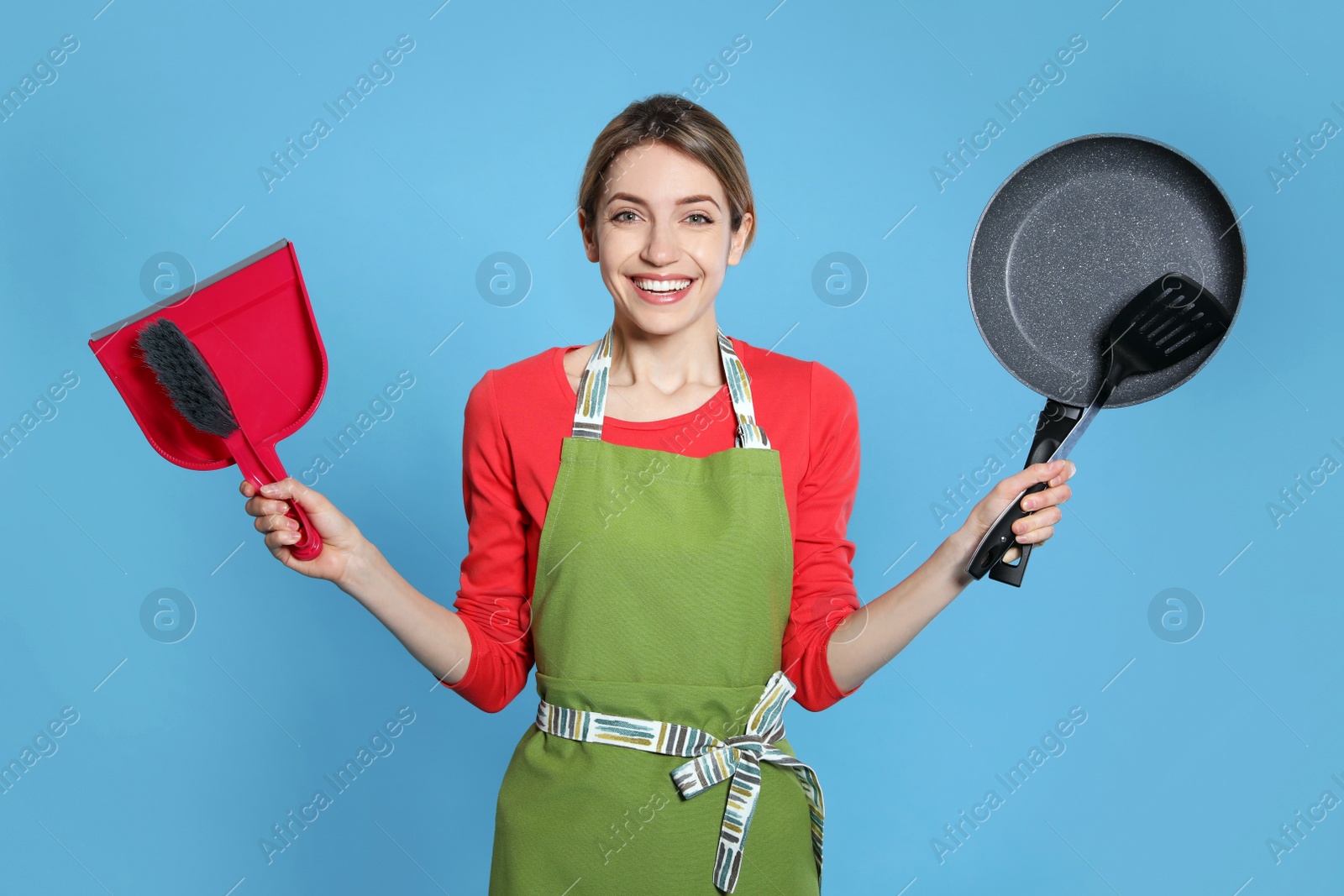 Photo of Young housewife with dustpan, brush, frying pan and spatula on light blue background