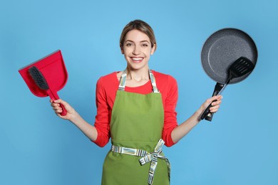 Photo of Young housewife with dustpan, brush, frying pan and spatula on light blue background