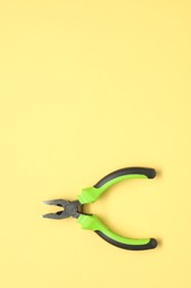 Photo of Combination pliers on yellow background, top view. Space for text