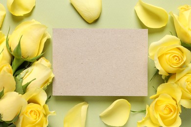 Beautiful yellow roses, petals and blank card on light olive background, flat lay. Space for text