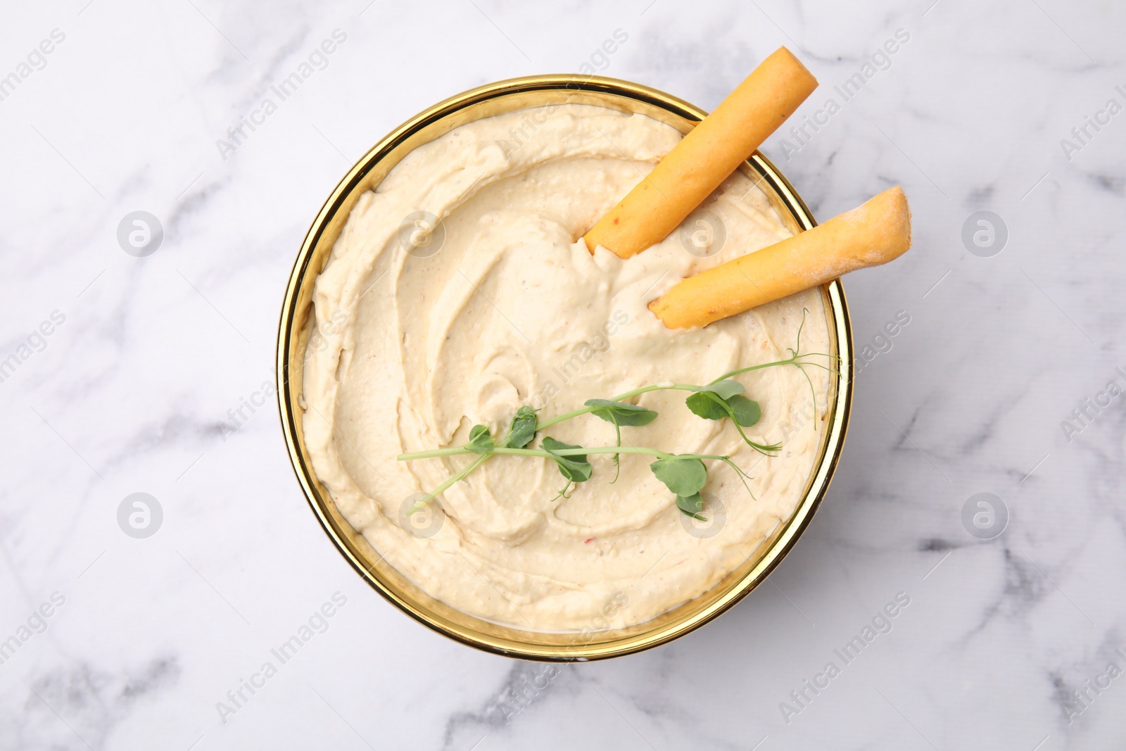 Photo of Delicious hummus with grissini sticks on white marble table, top view