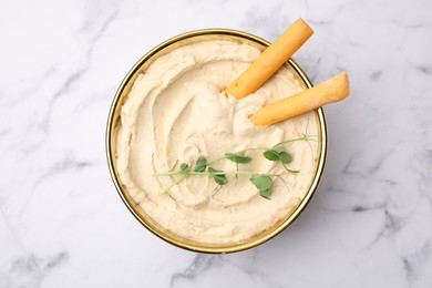 Delicious hummus with grissini sticks on white marble table, top view