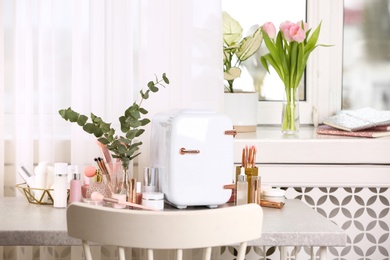 Photo of White mini cosmetics refrigerator and skin care products on table