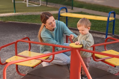 Photo of Happy nanny and cute little boy on carousel outdoors