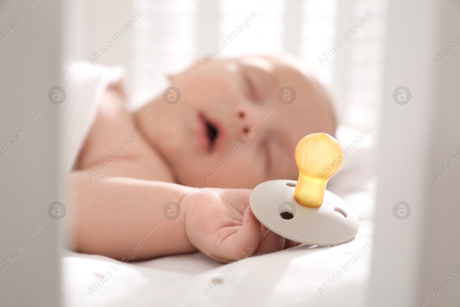 Photo of Cute little baby sleeping in crib, focus on hand with pacifier