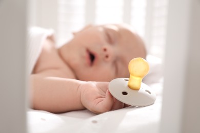 Cute little baby sleeping in crib, focus on hand with pacifier