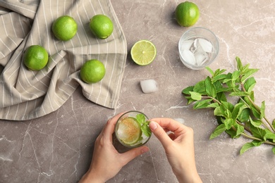 Young woman making delicious mint julep cocktail at table