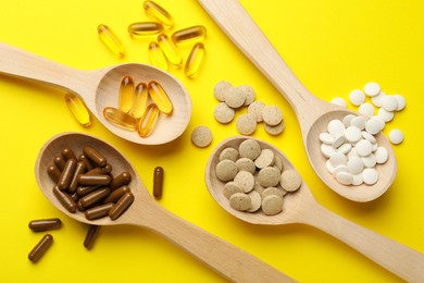 Photo of Wooden spoons and different dietary supplements on yellow background, flat lay