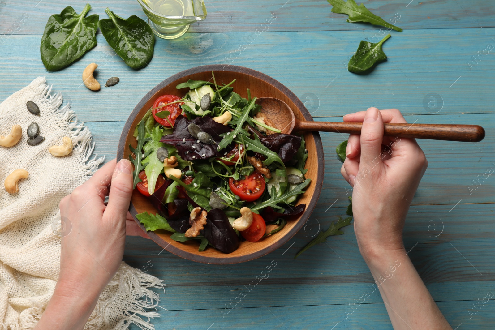 Photo of Woman with tasty fresh vegetarian salad at light blue wooden table, top view